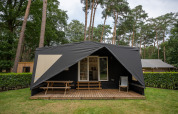 Safari Cooc Tent Deluxe im Familiepark Goolderheide, Belgien, mit Holzveranda und Picknickbank im Grünen.
