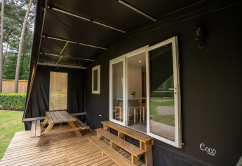 Terraza de la tienda safari Cooc Tent Deluxe con mesa de picnic en Familiepark Goolderheide, Bélgica.