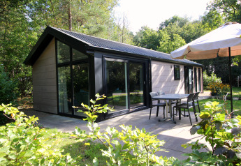 Terrasse extérieure du lodge Velthorst Hottub entourée de verdure avec table, chaises et parasol.