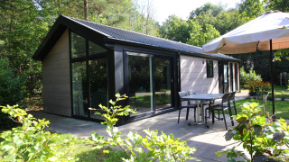 Buitenterras van Velthorst Hottub lodge in groene tuin met tafel, stoelen en grote parasol.