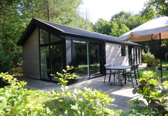 Buitenterras van Velthorst Hottub lodge in groene tuin met tafel, stoelen en grote parasol.