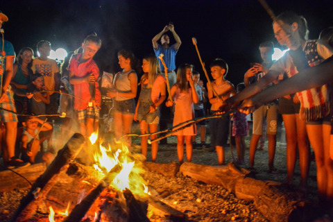 Kinderen en volwassenen roosteren marshmallows rond een kampvuur op een zomerse avond in La Draille.