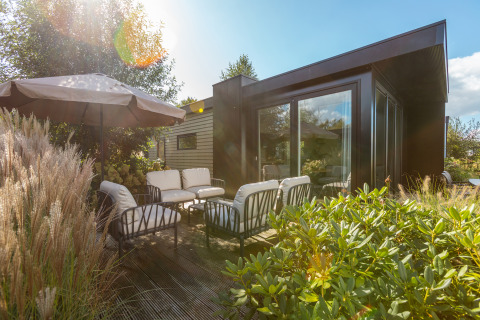 Sunlit patio at Vakantiechalet comfort+ with outdoor seating and umbrella at De Wiedense Meren, Netherlands.