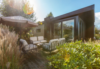 Patio soleggiato al Vakantiechalet comfort+ con sedute esterne e ombrellone a De Wiedense Meren, Paesi Bassi.