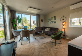 Moderne stue i Vakantiechalet comfort+ ved Vakantiepark De Wiedense Meren med store vinduer og hyggelig indretning.