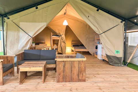 Indretning af safari telt med træmøbler, sovepladser, spisebord og moderne bekvemmeligheder.
