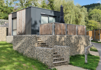 Tiny house moderne à façade bois, escaliers de pierre et terrasse, entourée de verdure et d’arbres.
