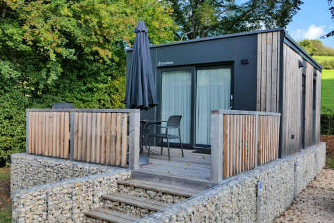 Moderne tiny house aan Kohnenhof in Luxemburg met houten terras, stoelen en een zwarte parasol.