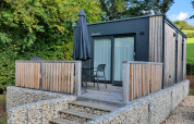 Modern tiny house at Kohnenhof in Luxembourg with wooden terrace, patio chairs and a black umbrella.