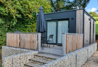 Moderne tiny house aan Kohnenhof in Luxemburg met houten terras, stoelen en een zwarte parasol.