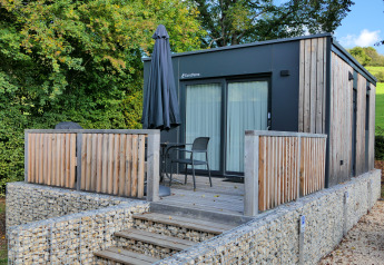 Tiny house moderne au Kohnenhof au Luxembourg avec terrasse en bois, fauteuils de jardin et un parasol noir.