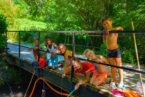 Kinderen vissen plezierig vanaf een brug op een zonnige dag in het vakantiepark La Draille, Occitanië, Frankrijk.