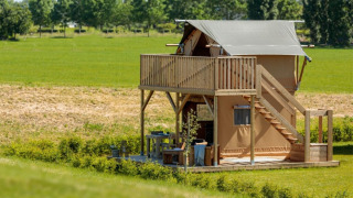 Une tente de glamping moderne avec balcon supérieur et coin salon extérieur, dans un paysage rural verdoyant.