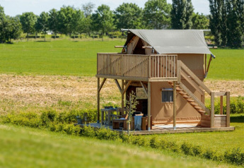 Una tenda glamping moderna con balcone superiore e zona relax esterna, immersa in un paesaggio rurale verde.