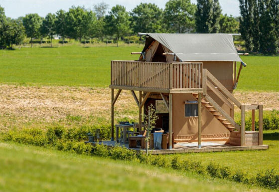 Une tente de glamping moderne avec balcon supérieur et coin salon extérieur, dans un paysage rural verdoyant.