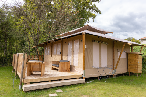 Safaritent Stardust 40 Family Lodge met houten terras, tuinmeubels en groene omgeving onder een bewolkte lucht.