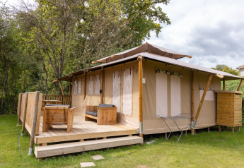 Tente safari Stardust 40 Family Lodge avec terrasse en bois, mobilier d'extérieur et verdure environnante.
