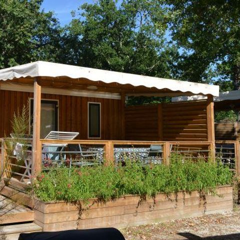 Stacaravan Premium Clim presso Flower Camping La Canadienne in Francia con terrazza in legno e piante verdi.