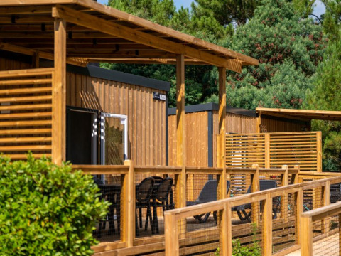 Buitenfoto van een glamping accommodatie met houten terras, ligstoelen en bomen op de achtergrond.
