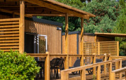 Outdoor photo of a glamping accommodation featuring a wooden terrace, lounge chairs, and greenery behind.