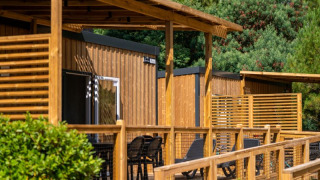 Outdoor photo of a glamping accommodation featuring a wooden terrace, lounge chairs, and greenery behind.