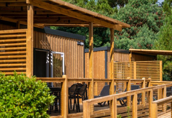 Buitenfoto van een glamping accommodatie met houten terras, ligstoelen en bomen op de achtergrond.