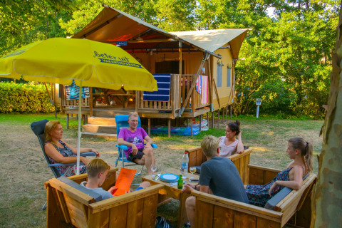 Gezin zit samen buiten op houten stoelen bij een safaritent in vakantiepark La Draille, Occitanië, Frankrijk.