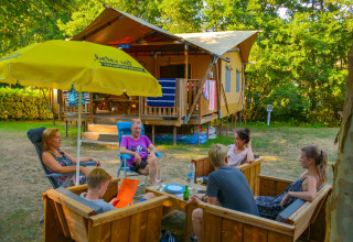 Gezin zit samen buiten op houten stoelen bij een safaritent in vakantiepark La Draille, Occitanië, Frankrijk.
