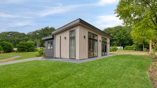 Modern lodge named Heideveld with large windows, lush green lawn, and trees under a blue sky.