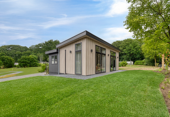 Modern lodge named Heideveld with large windows, lush green lawn, and trees under a blue sky.