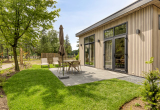 Patio exterior de una moderna cabaña en Bospark Ede, Países Bajos, con muebles de jardín y césped verde.