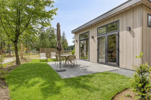 Außenterrasse einer modernen Lodge im Bospark Ede, Niederlande, mit Gartenmöbeln und grüner Rasenfläche.