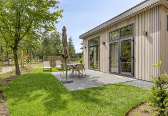 Außenterrasse einer modernen Lodge im Bospark Ede, Niederlande, mit Gartenmöbeln und grüner Rasenfläche.