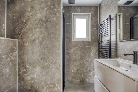 Bagno moderno con pareti in marmo, finestra, lavabo e scaldasalviette nero presso Heideveld, Bospark Ede, Paesi Bassi.