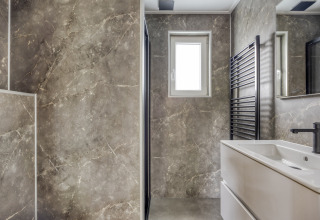 Modern bathroom with marble walls, window, sink and black towel rail at Heideveld lodge, Bospark Ede, Netherlands.