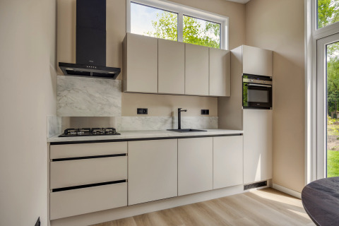 Cocina moderna en la cabaña Heideveld de Bospark Ede, Países Bajos, con armarios claros y ventanas grandes.