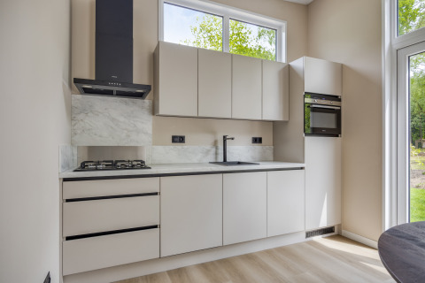 Cocina moderna en la cabaña Heideveld de Bospark Ede, Países Bajos, con armarios claros y ventanas grandes.