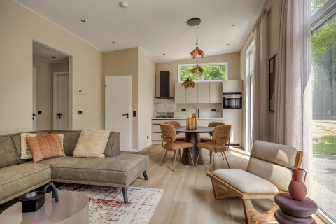 Salón de lodge moderno y luminoso con cocina abierta y grandes ventanales en Heideveld, Bospark Ede, Países Bajos.