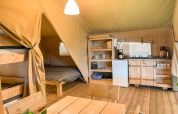Interior de una tienda safari con cocina, mesa de comedor, litera y cama doble en Glyngore Camping.