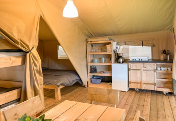 Interior de una tienda safari con cocina, mesa de comedor, litera y cama doble en Glyngore Camping.