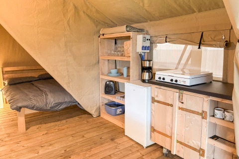 Innenraum eines Safarizeltes mit Bett, Küchenzeile, Kühlschrank und Kaffeemaschine bei Glyngore Camping.