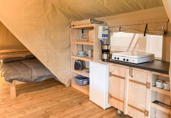 Innenraum eines Safarizeltes mit Bett, Küchenzeile, Kühlschrank und Kaffeemaschine bei Glyngore Camping.