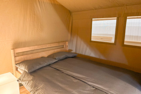 Double bed inside a cozy safari tent with windows at Glyngore Camping, Denmark, flooded with warm light.