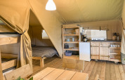 Intérieur d'une tente safari avec cuisine, table à manger, lits superposés et lit double à Himmerland camping.