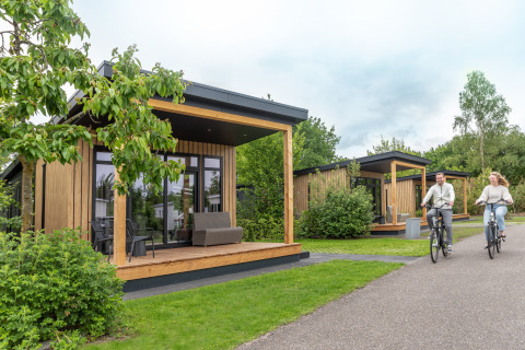 Koppel fietst voor Sunlodge in Holiday Park 't Rheezerwold in Nederland, moderne houten lodges in groene omgeving.
