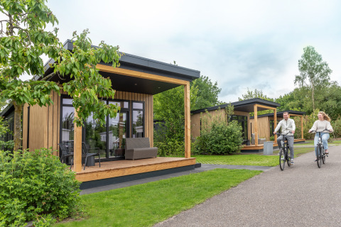 Stel fietst langs Sunlodge bij Holiday Park 't Rheezerwold in Nederland, moderne houten lodges in het groen.