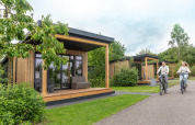 Stel fietst langs Sunlodge bij Holiday Park 't Rheezerwold in Nederland, moderne houten lodges in het groen.