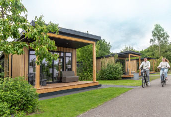 A couple rides bicycles near Sunlodge at Holiday Park 't Rheezerwold in the Netherlands, modern wooden lodges.
