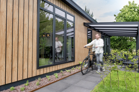Man met fiets voor Sunlodge bij Holiday Park 't Rheezerwold in Nederland, met moderne houten gevel.