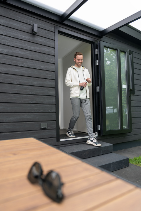 Man verlaat Sunlodge bij Holiday Park 't Rheezerwold, zonnebril op houten tafel op de voorgrond.